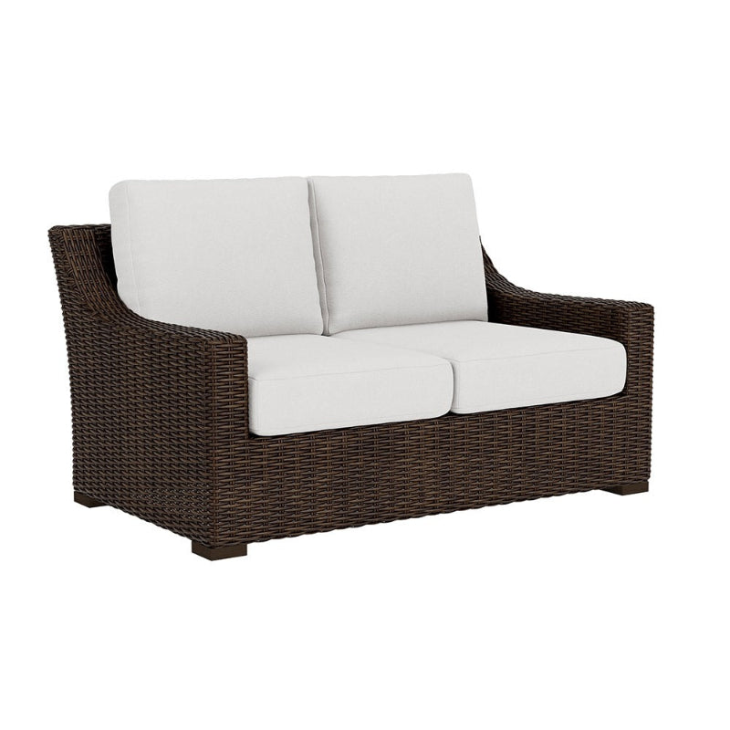 Brown wicker outdoor sofa with white cushions on a white background