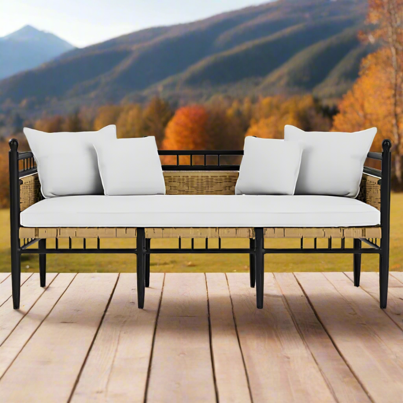 Wicker bench with white cushions on a wooden deck with a mountainous landscape in the background