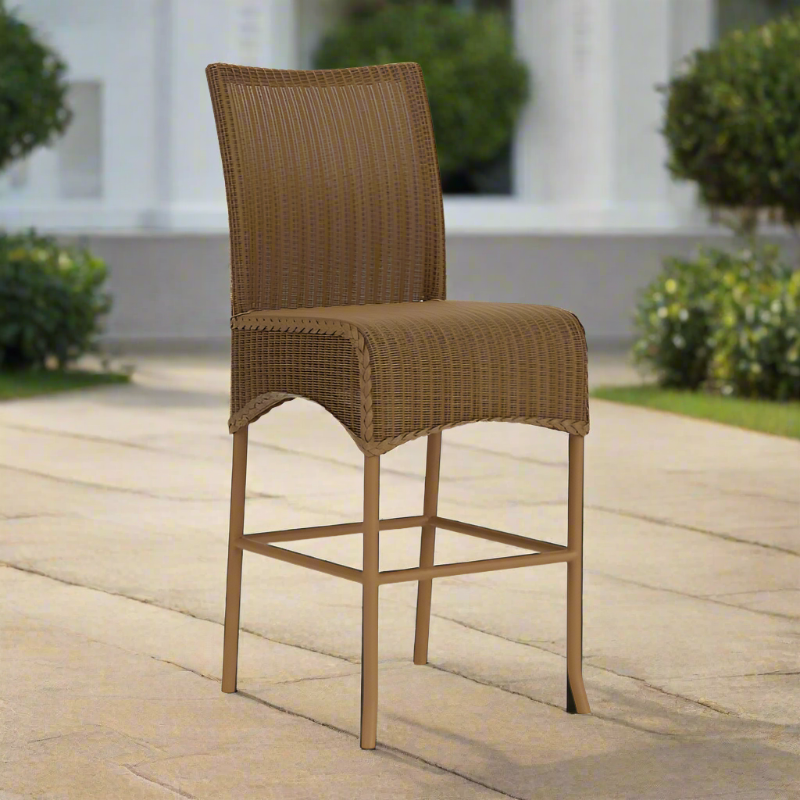 Brown wicker bar stool on a wooden deck with a garden background