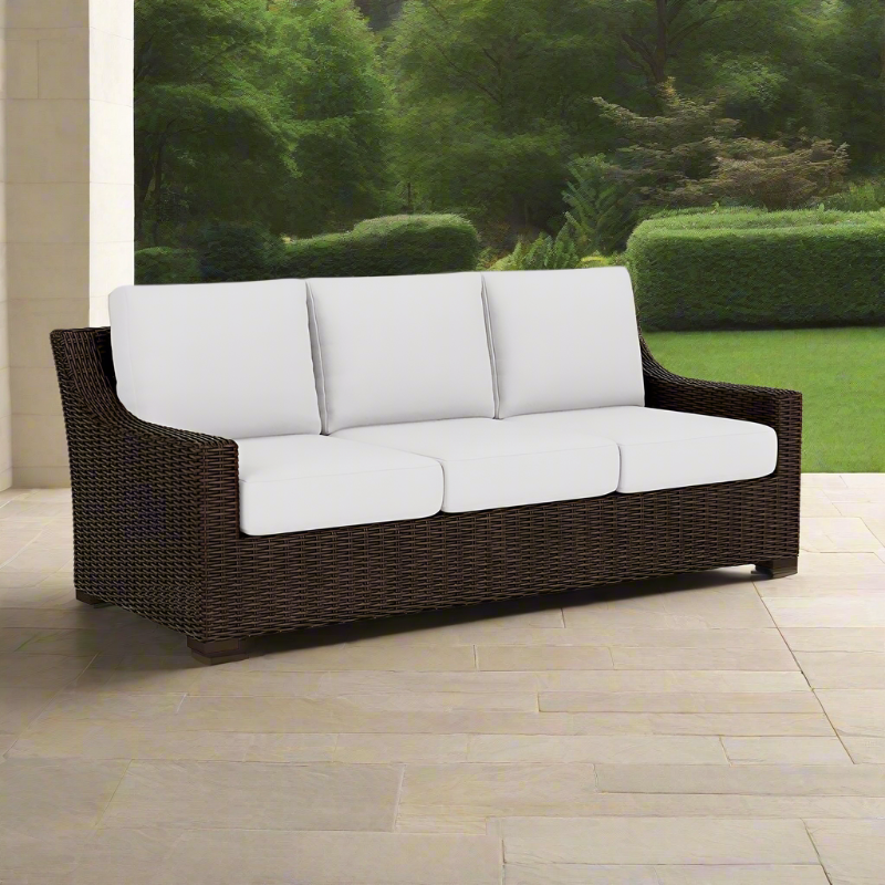 Brown wicker outdoor sofa with white cushions on a patio