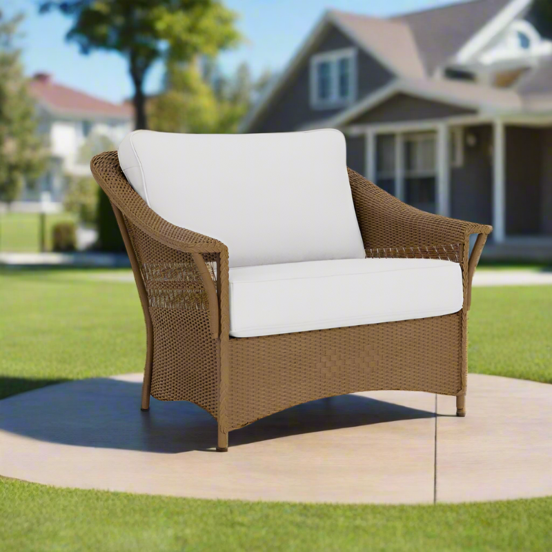 Brown wicker chair with white cushions on a patio in a residential backyard.