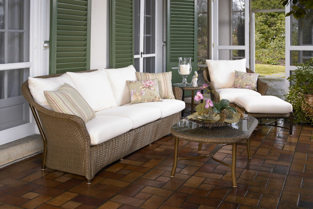 Outdoor patio set with wicker furniture and white cushions on a wooden floor.