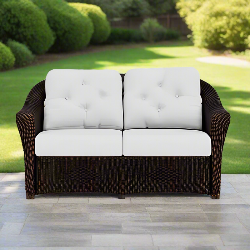 Brown wicker outdoor sofa with white cushions on a patio