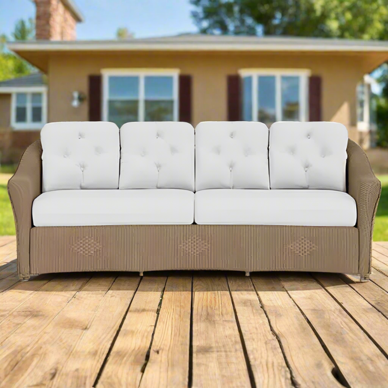 Beige outdoor sofa with white cushions on a wooden deck in front of a house.
