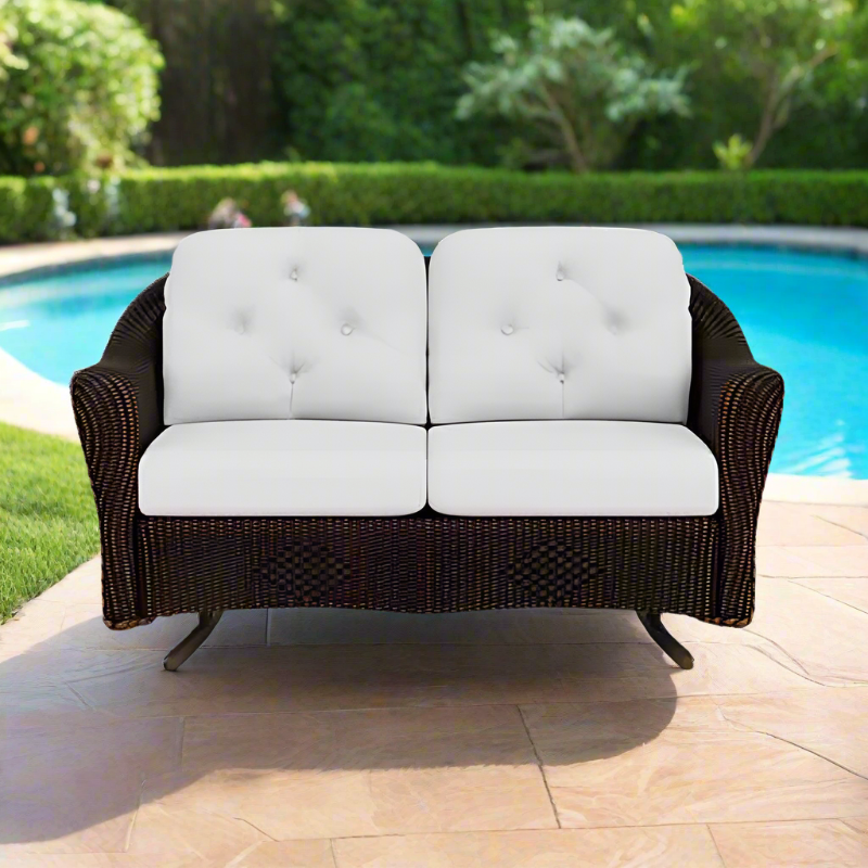 Wicker outdoor loveseat with white cushions by a pool