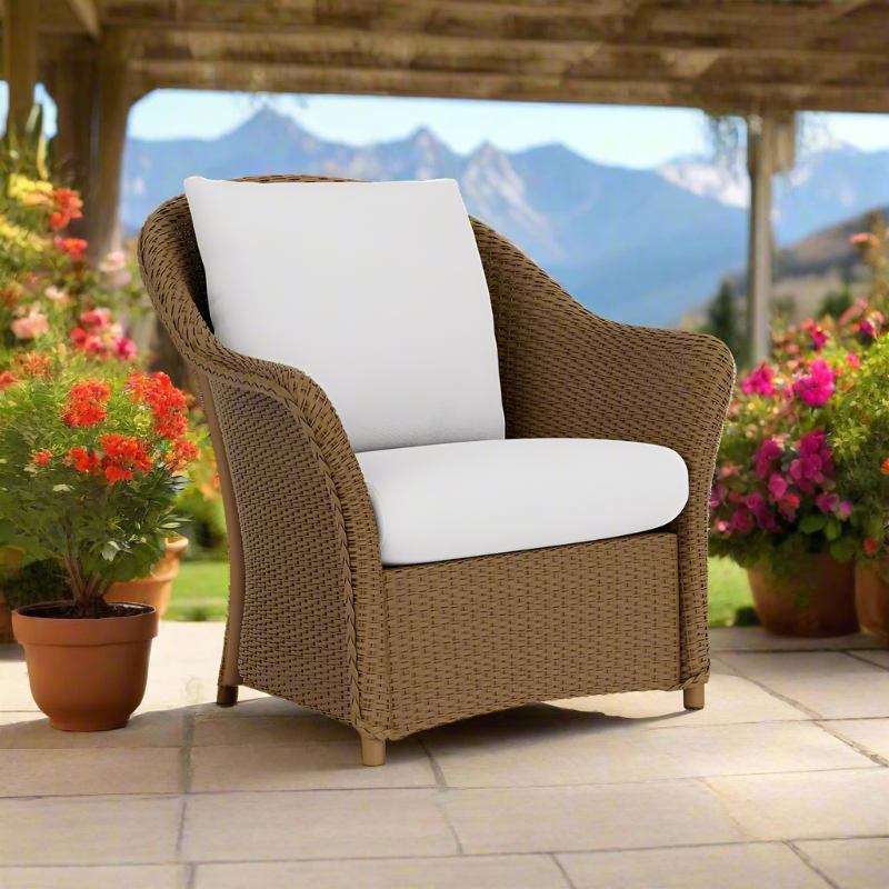 Wicker chair with white cushions on a patio with flowers and mountains in the background