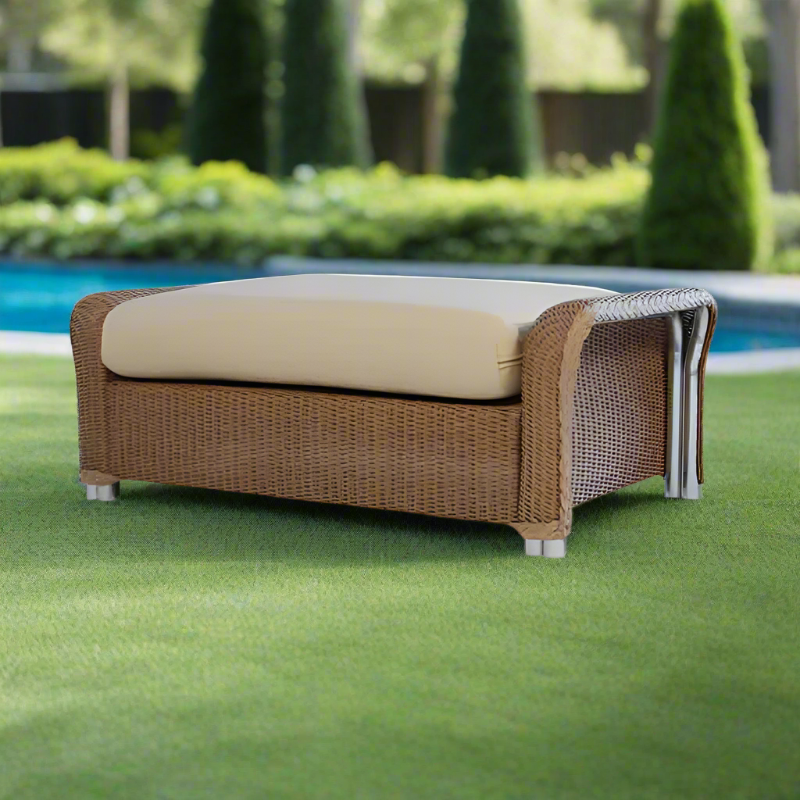 Wicker outdoor bench with beige cushion on a grassy area near a pool