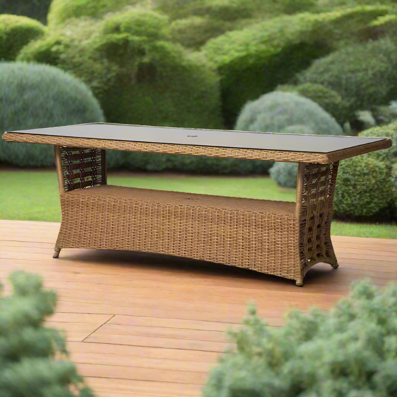 Wicker outdoor table with a glass top on a wooden deck surrounded by greenery