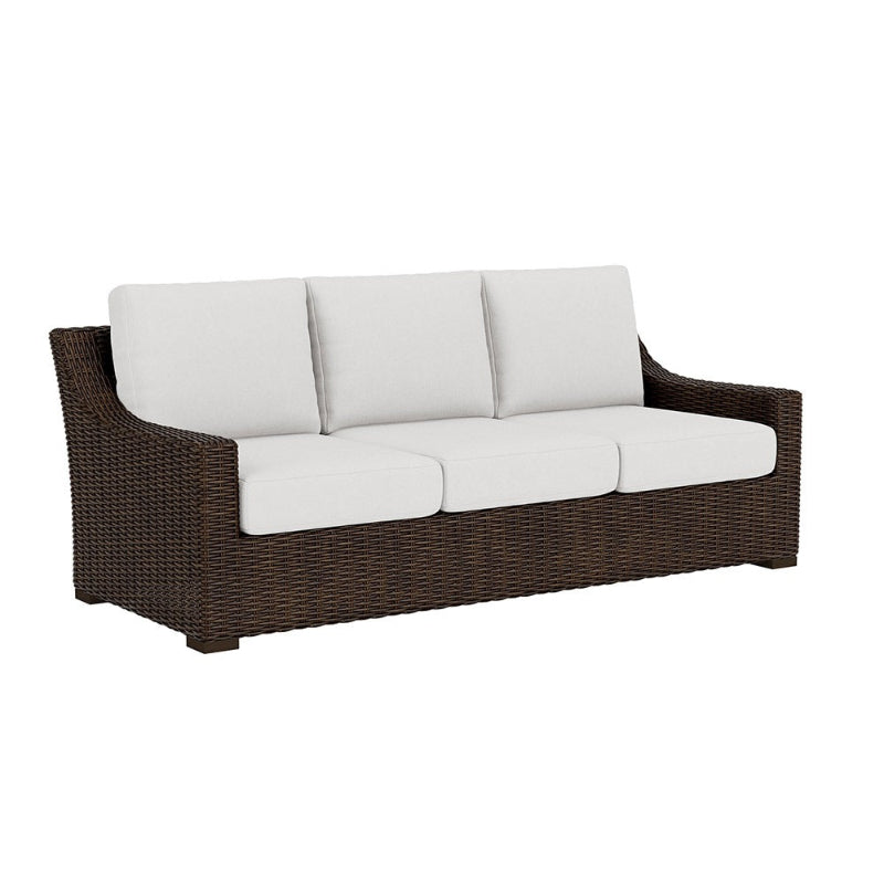 Brown wicker outdoor sofa with white cushions on a white background