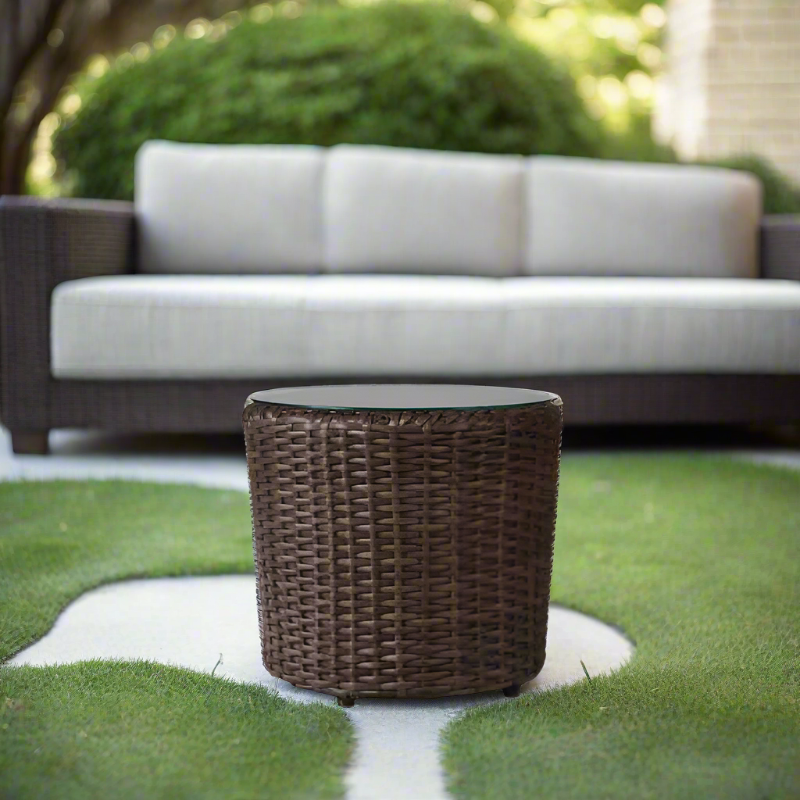 Wicker side table on a grassy area with a blurred outdoor sofa in the background