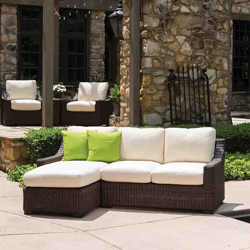 Outdoor patio furniture set with a sectional sofa and chairs against a stone wall.