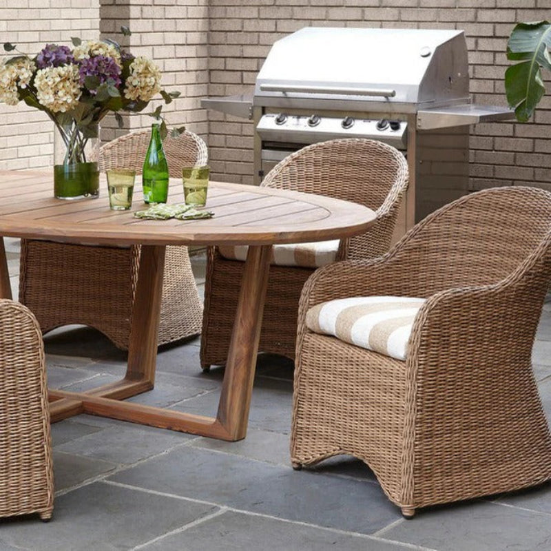 Outdoor patio set with wooden table and wicker chairs on a stone patio, featuring a grill in the background.