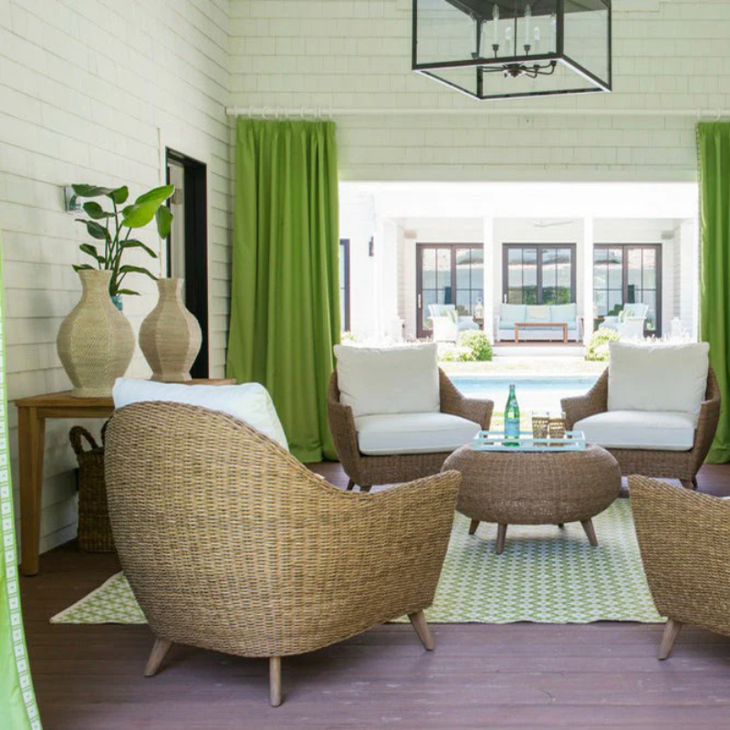 Outdoor patio with wicker furniture, green curtains, and a pool view.