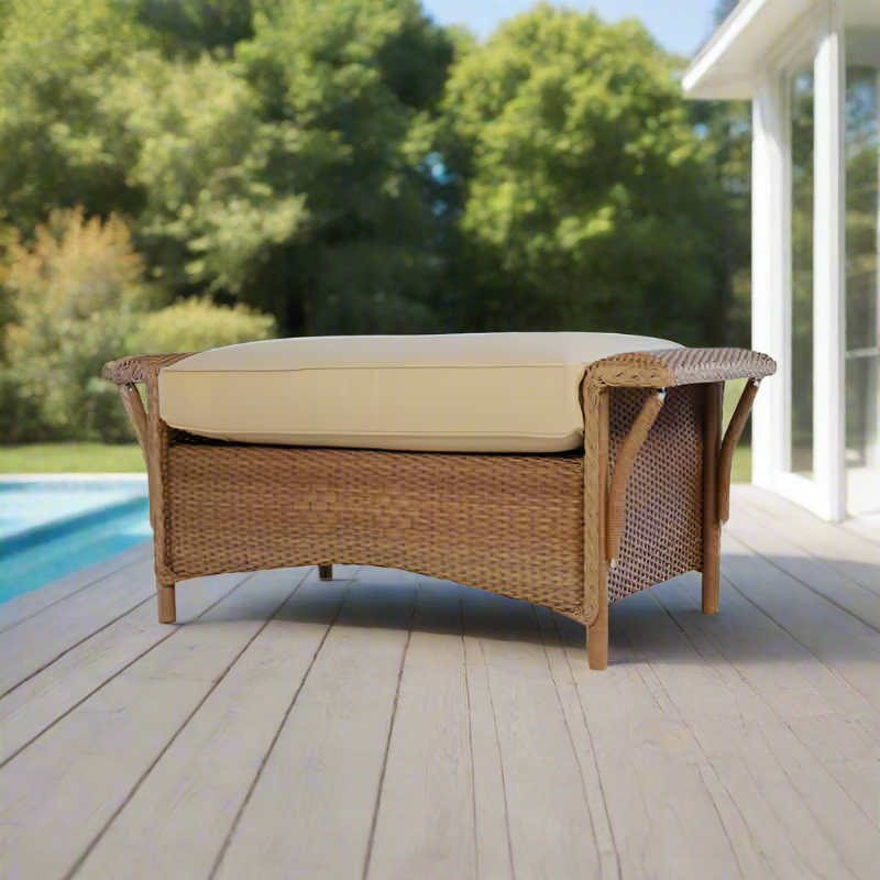 Wicker outdoor bench with beige cushion on a wooden deck by a pool