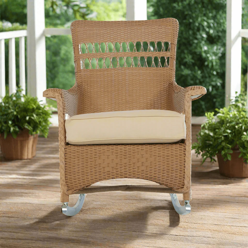 Wicker rocking chair with beige cushion on a wooden deck with plants in the background