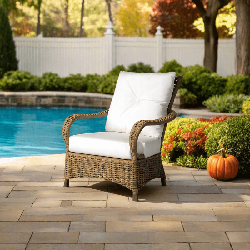 Brown wicker chair with white cushion by a poolside with garden and pumpkin in the background