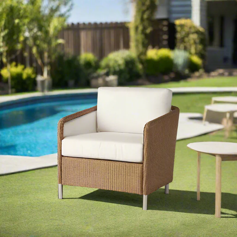 Brown wicker chair with white cushions by a pool in a garden setting