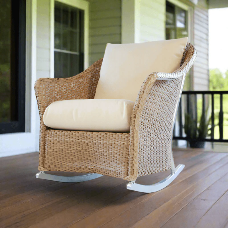 Wicker rocking chair with beige cushions on a wooden porch