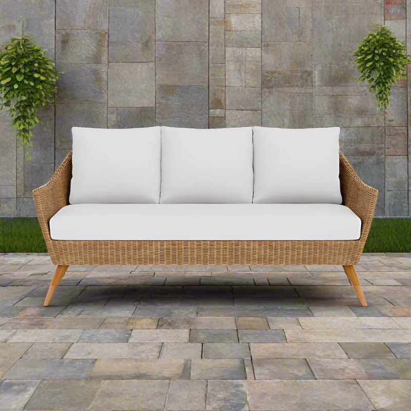 Wicker outdoor sofa with white cushions against a stone wall.