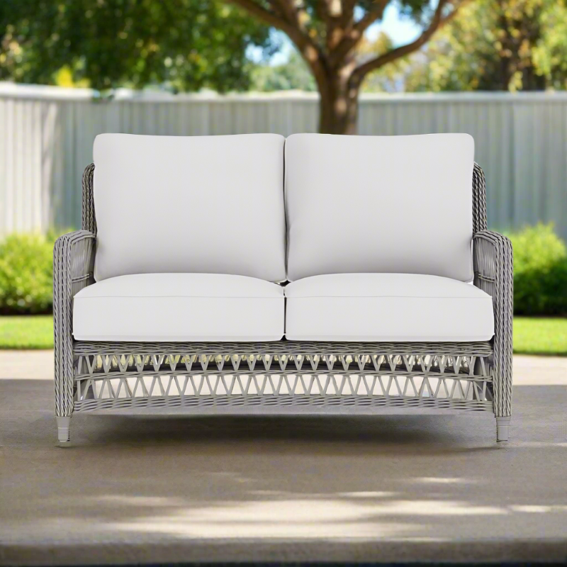 Outdoor wicker loveseat with white cushions on a patio