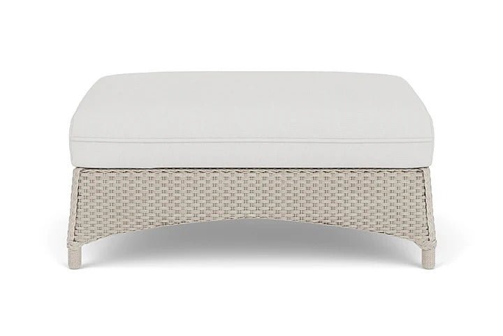 Wicker ottoman with a white cushion on a white background