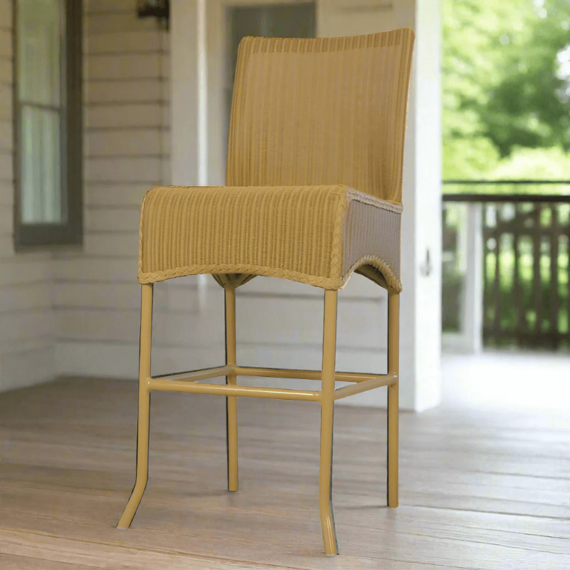 Yellow wicker bar stool on a wooden deck with a blurred outdoor background