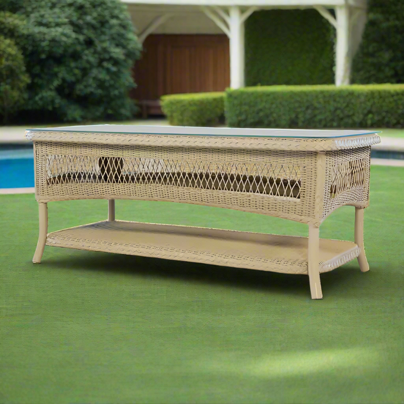 Wicker coffee table on a green lawn with a pool and garden in the background