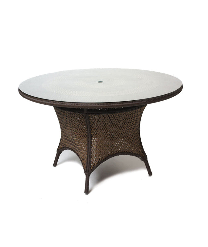 A round Lloyd Flanders wicker dining table with a glass top and umbrella opening, featuring a brown synthetic woven wicker base and a white glass top.