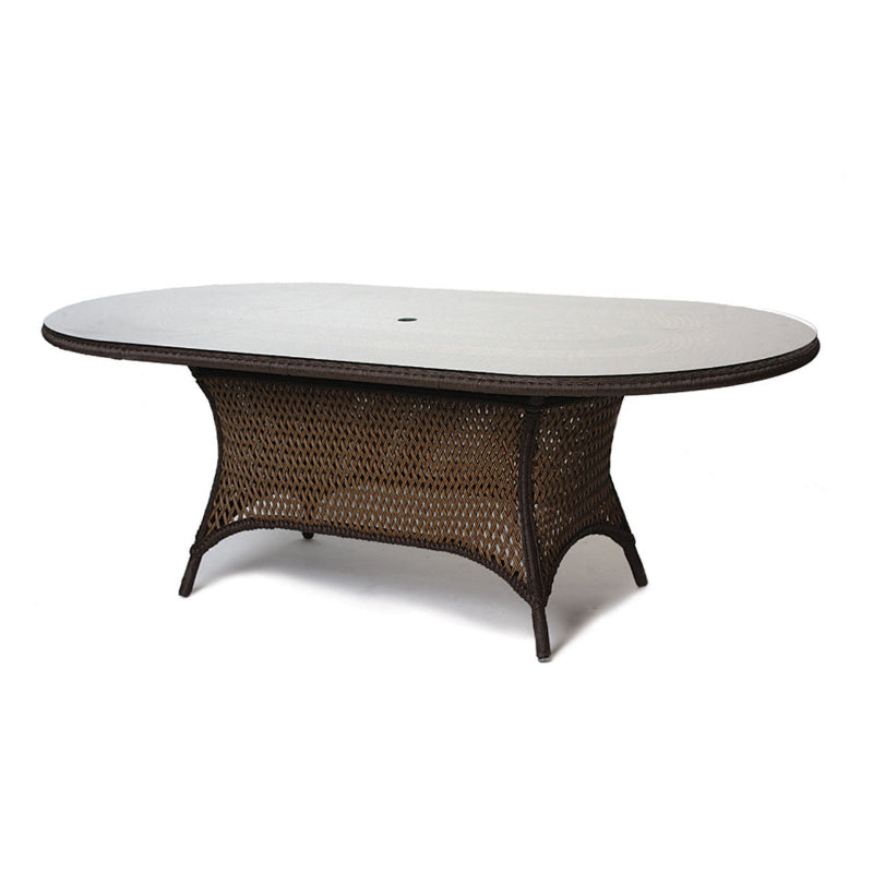 An oval-shaped Lloyd Flanders Grand Traverse wicker dining table with a lay on glass top, displayed against a white background.